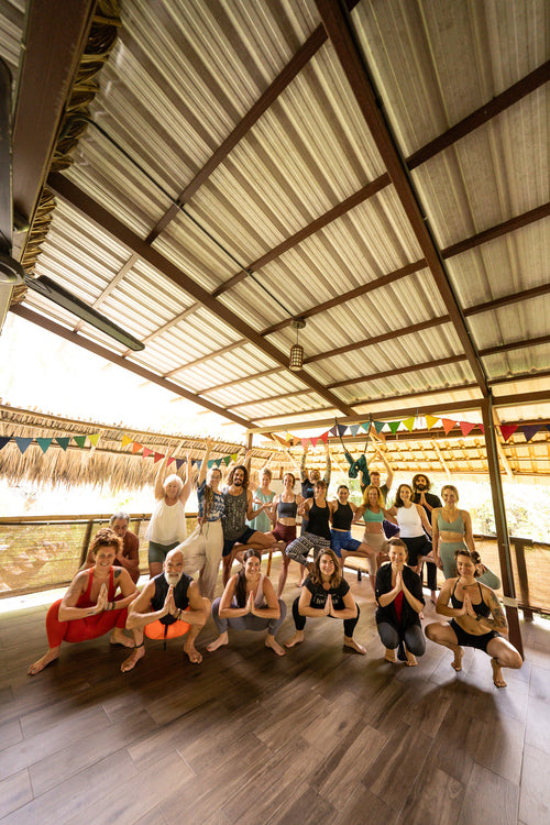 Group of people practicing yoga on a wooden deck with a thatched roof.