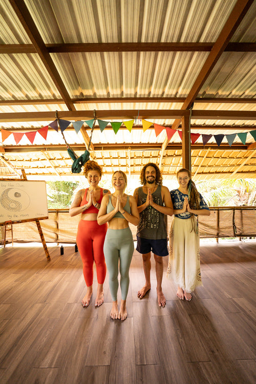 Four retreat participants in Costa Rica standing in a prayer-like pose in a studio with yoga imagery and festive flags.
