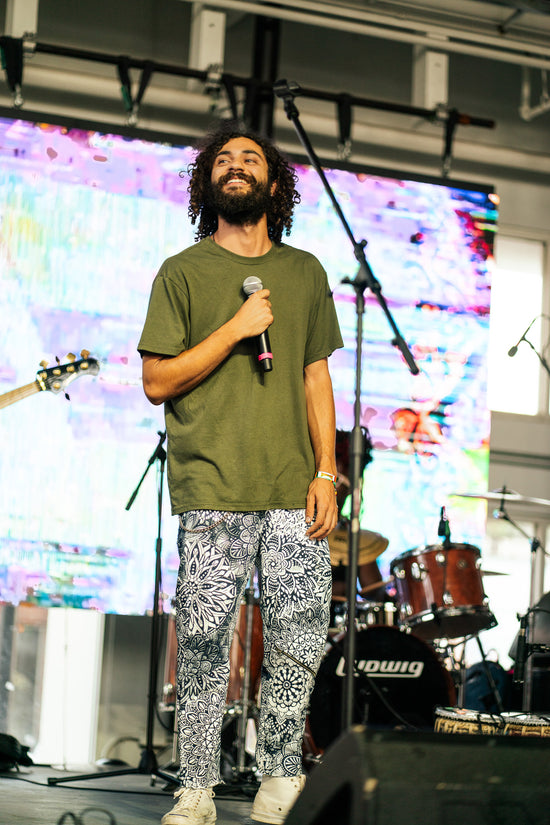 Man on stage with microphone in front of colorful screen and musical instruments